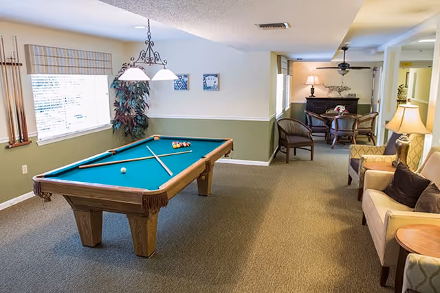 A bright communal room with a pool table, seating area, and a small dining table.