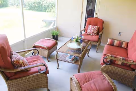 Sunlit screened porch with red-cushioned wicker chairs around a glass coffee table.