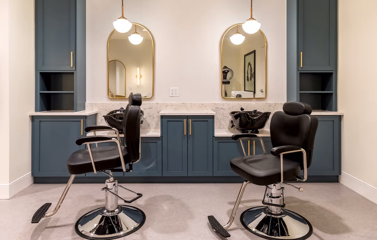 Two salon barber chairs facing sinks and mirrors in a small hair-washing station with blue cabinetry.