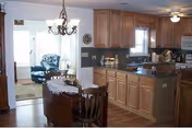 Open-plan kitchen with wooden cabinets and an island adjoining a dining table and a sunlit living area with armchairs.