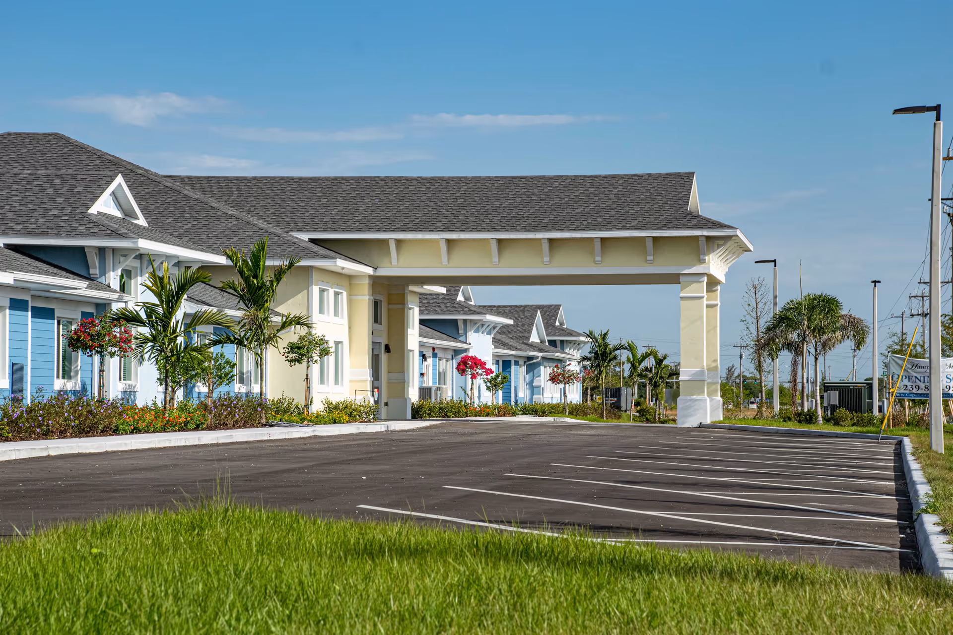 Covered entrance and adjacent parking lot of a low-rise senior living building with palm trees and colorful facades.