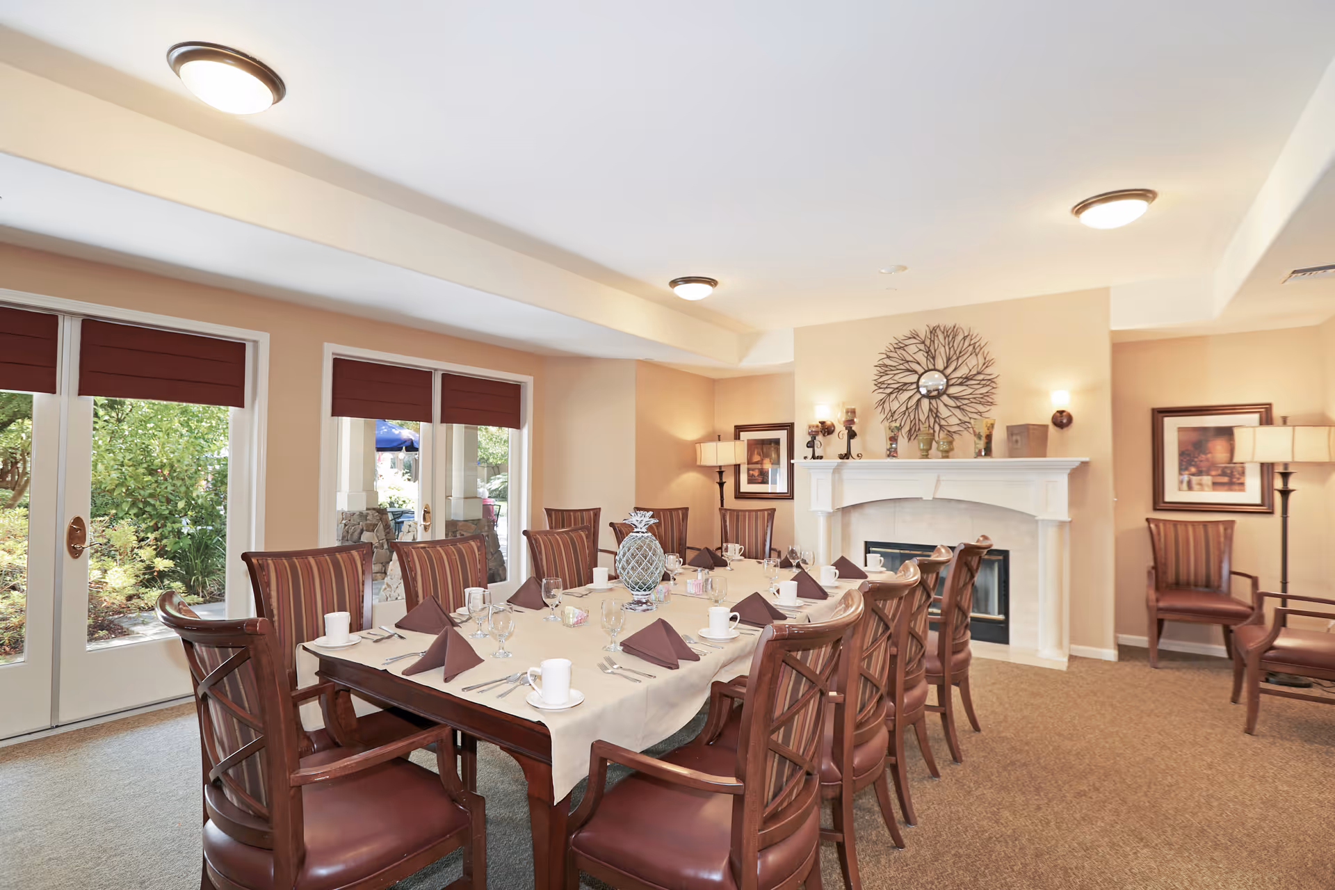 A formal dining room with a long table set for a meal, wooden chairs, and a fireplace with decorative wall art.