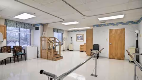 A spacious rehab room with parallel bars, wooden steps, chairs, and doors.