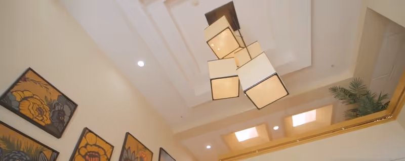 Ceiling view of a room with a modern chandelier featuring multiple square lampshades, recessed lighting, and framed floral artwork on the wall.