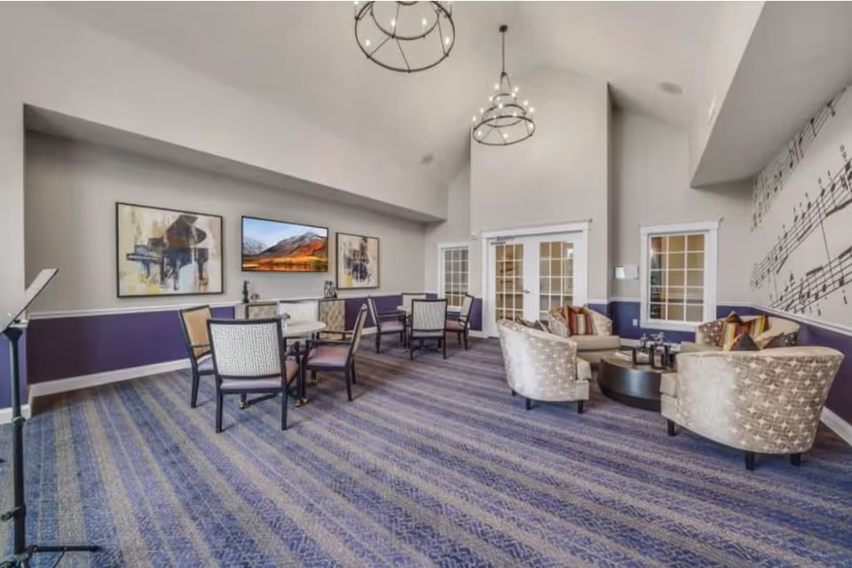 Spacious communal lounge with tables and upholstered chairs, patterned carpet, artwork, and a music-themed wall.