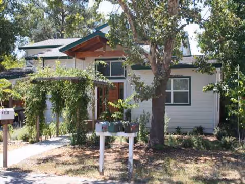 Single-story senior living facility front exterior with trees, a porch, and a mailbox.