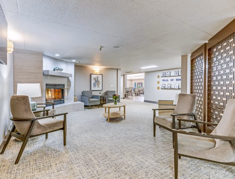 Cozy lounge area with armchairs and a coffee table arranged around a fireplace in a senior living facility.