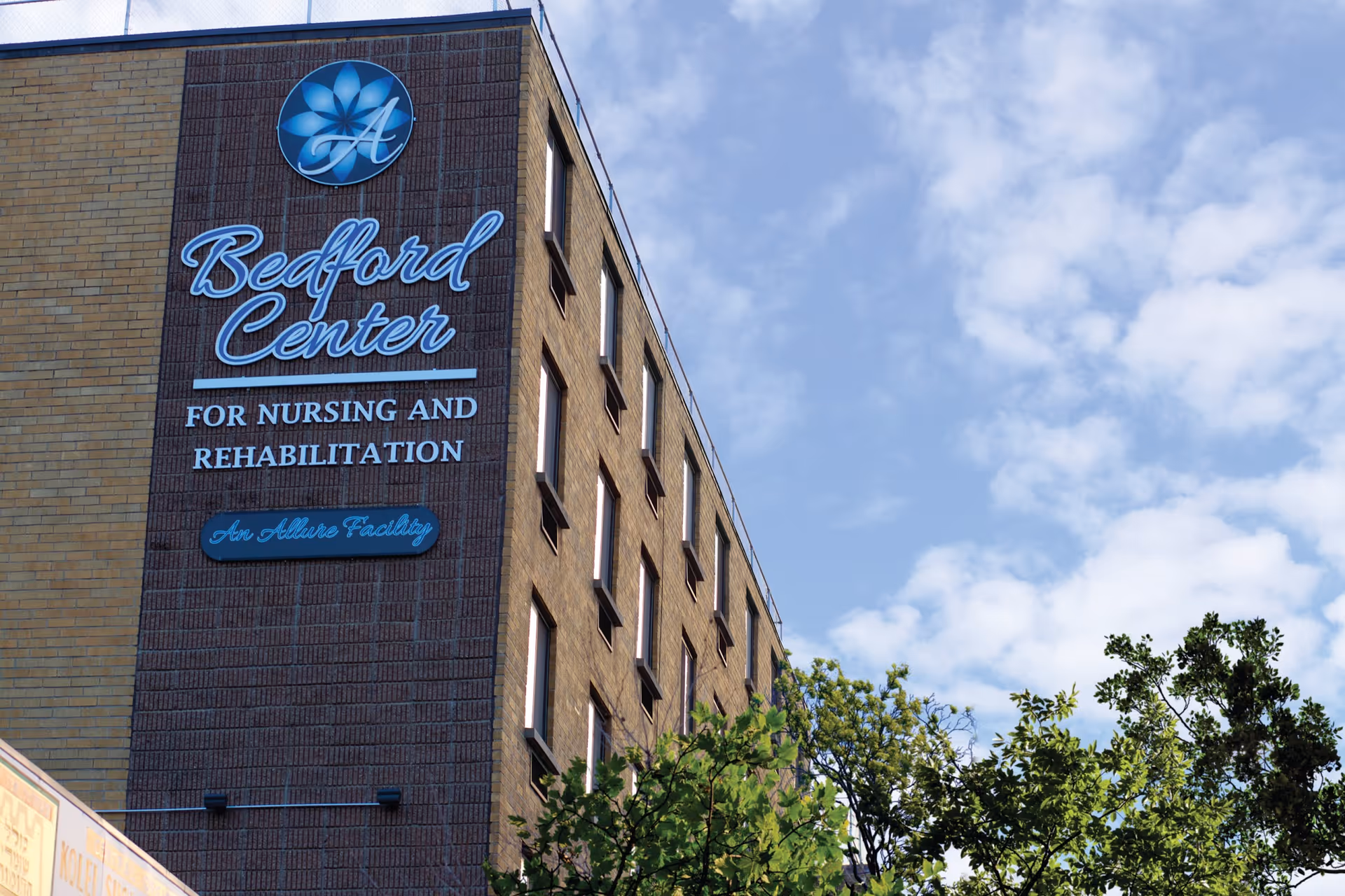 Exterior view of the Bedford Center for Nursing and Rehabilitation sign on a brick building facade against a blue sky.