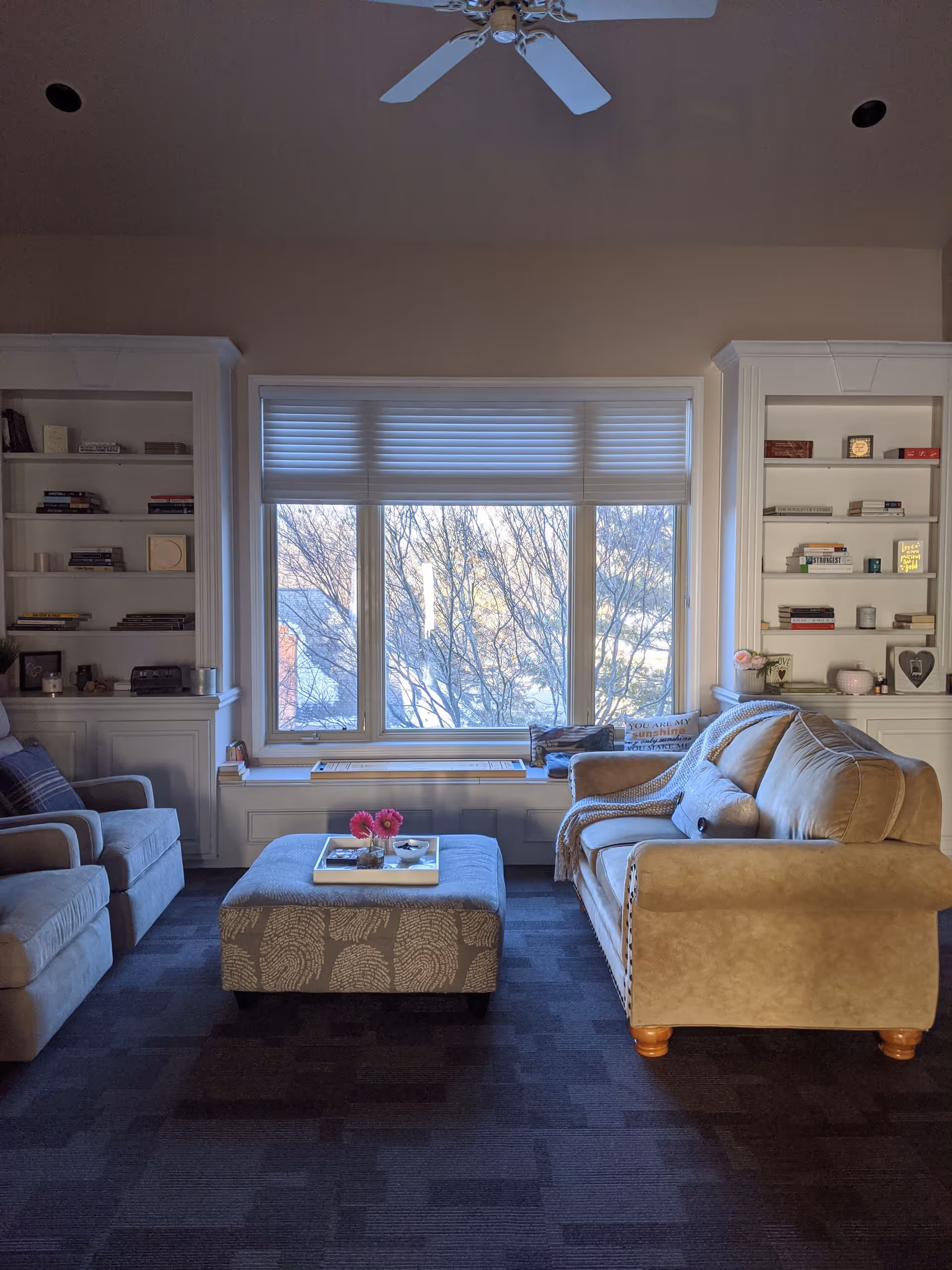 Living room with a sofa, armchairs, an ottoman-style coffee table and a large window flanked by built-in bookshelves.