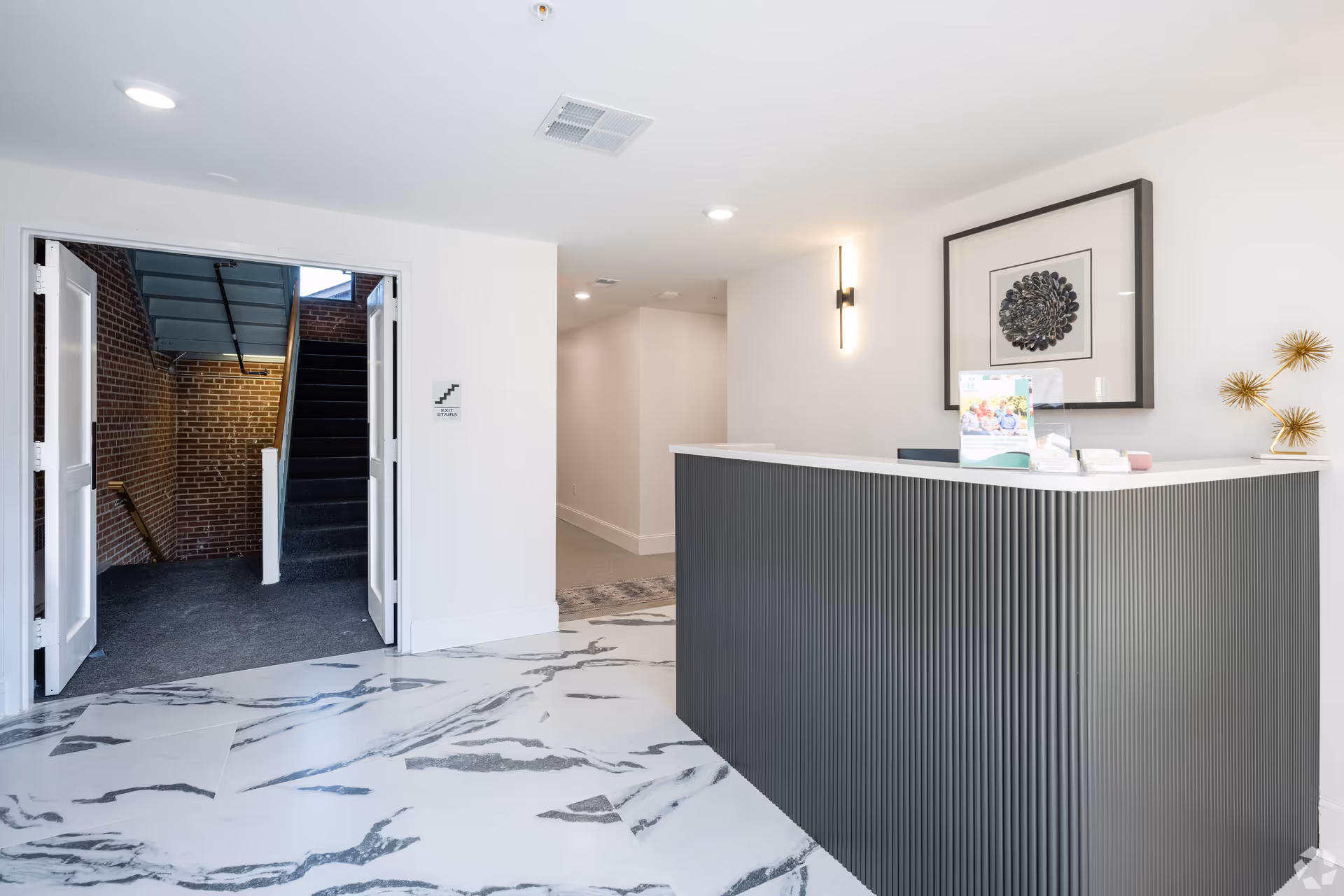 Bright modern lobby with a reception desk, marble-patterned floor, and an open doorway revealing brick stairs.