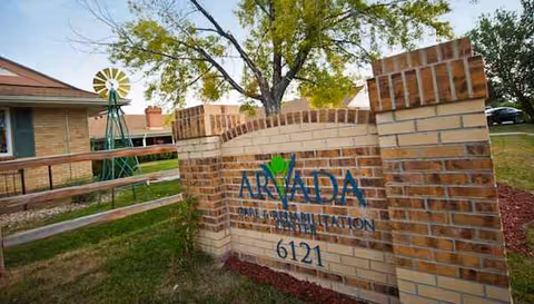 Brick entrance sign reading ARADA with address 6121, nearby windmill sculpture and trees.