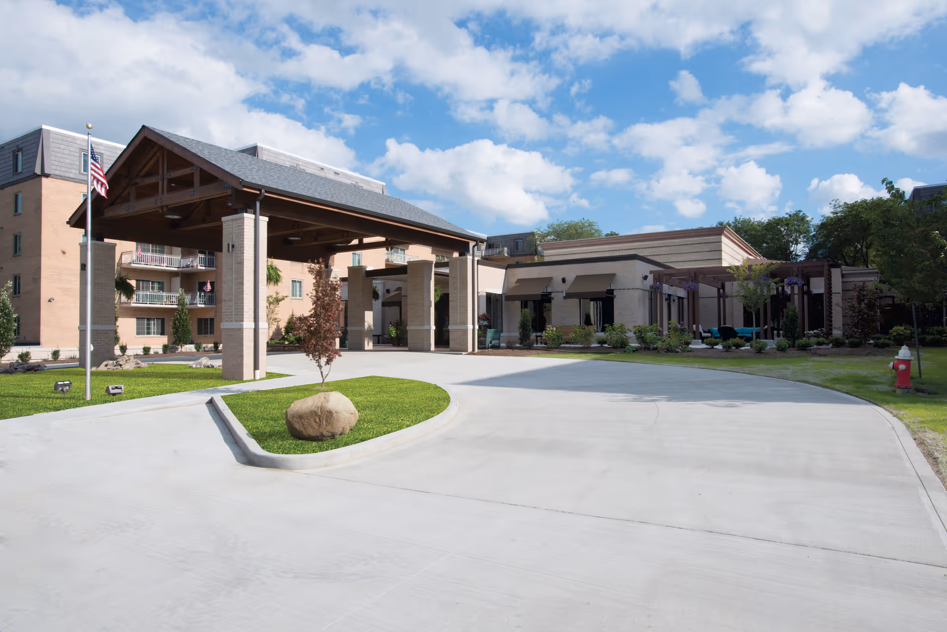 Front entrance of Lakeside at the Normandy showing a covered porte-cochere, driveway, flagpole, and surrounding landscaping.