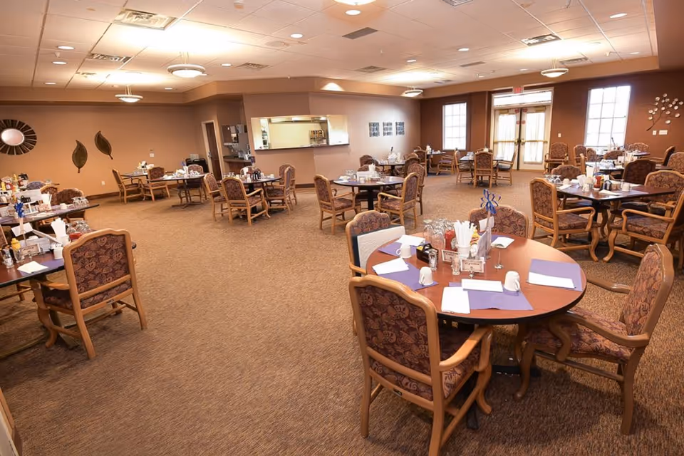 Spacious senior dining room with multiple round and rectangular tables set for meals.
