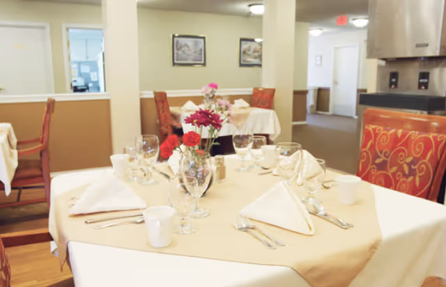 A neatly set dining table with folded napkins, glassware, and a floral centerpiece in a dining room.