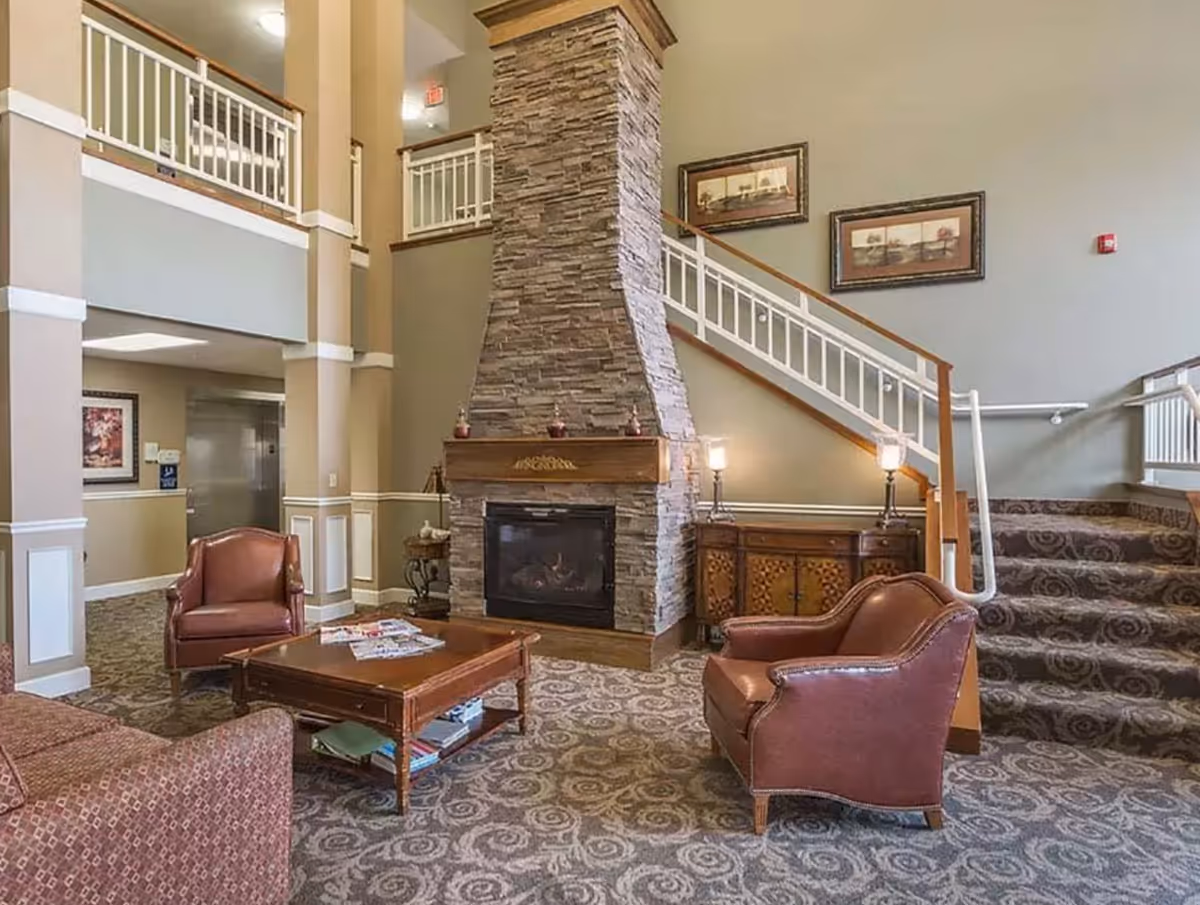 Spacious residential-style lobby with a stone fireplace, leather chairs, coffee table, and a carpeted staircase.