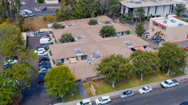 Aerial view of a single-story senior care facility with connected buildings, trees, and parked cars along the street.