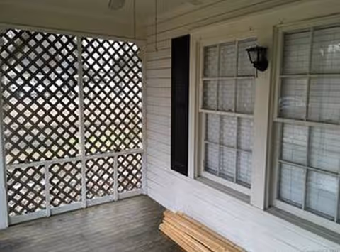 Front porch area with lattice screen, white siding, windows, and a wooden bench.