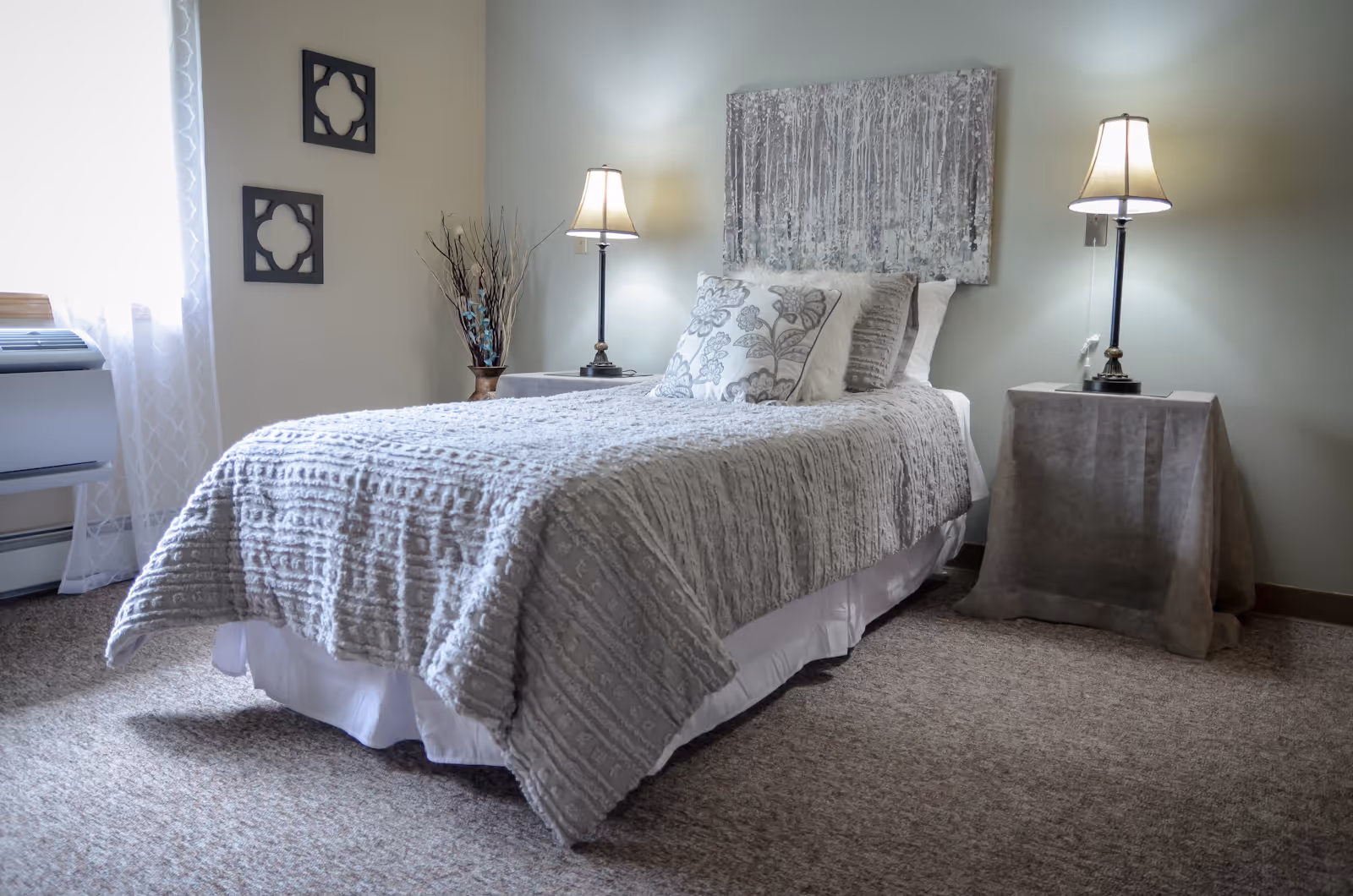 A neatly made single bed in a softly lit bedroom with two bedside lamps and neutral decor.