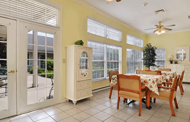 Sunlit dining area with a table and chairs, large windows, and a glass door opening to an outdoor patio.