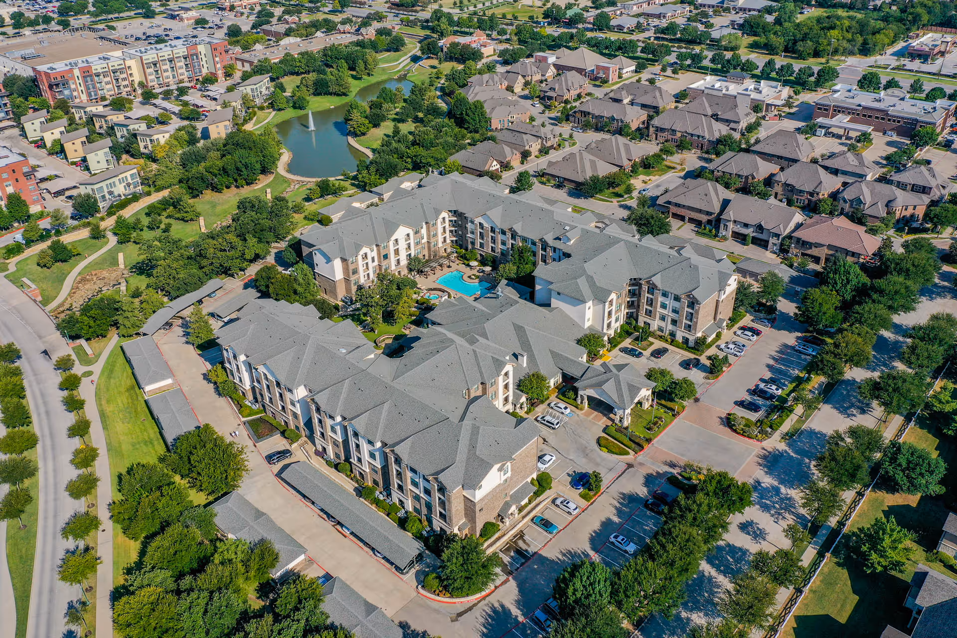 Aerial view of the Conservatory At Keller Town Center campus showing multiple connected residential buildings around a central courtyard pool, parking lots, trees and surrounding neighborhood.