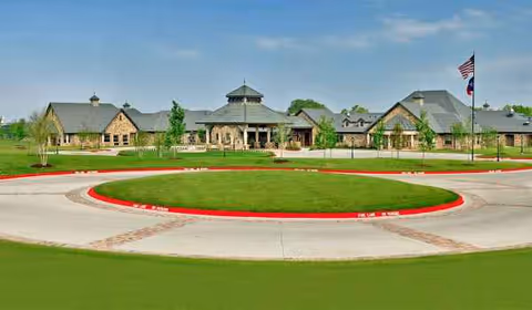 Exterior view of a large stone senior living facility with a circular driveway and flagpole.