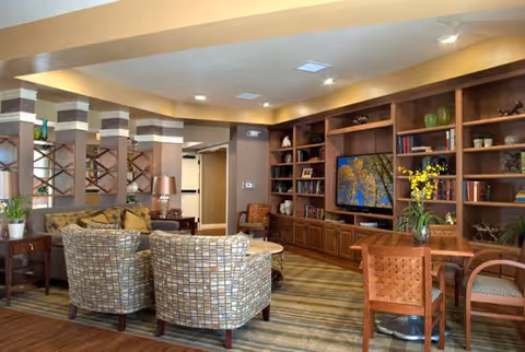 Comfortable lounge area with patterned armchairs, wooden built-in bookshelves and TV, and a small dining table.