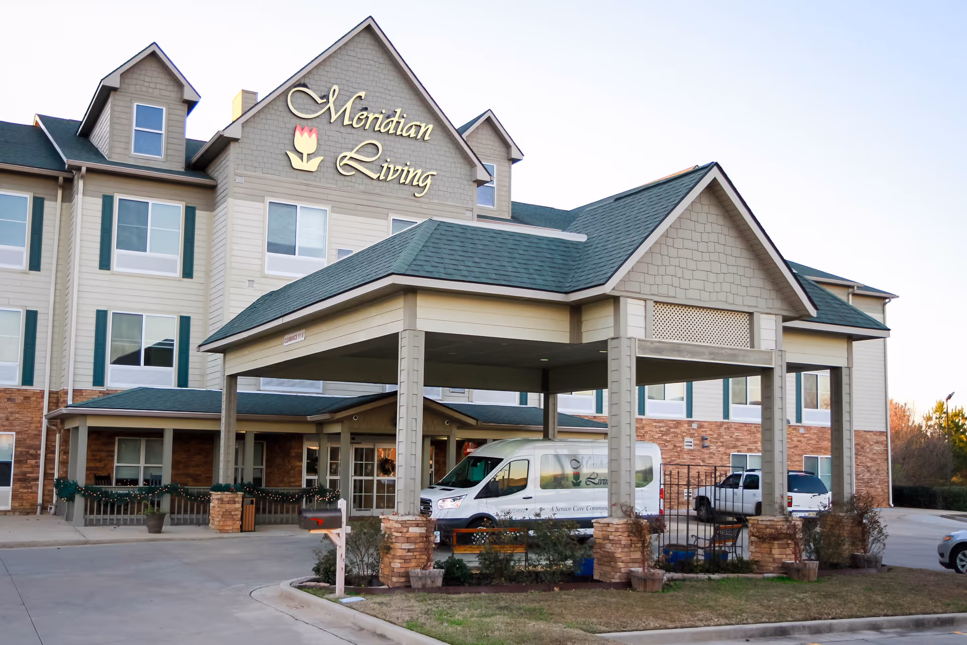 Front facade and entrance canopy of the Meridian Living senior living building with a van parked under the porte-cochere.