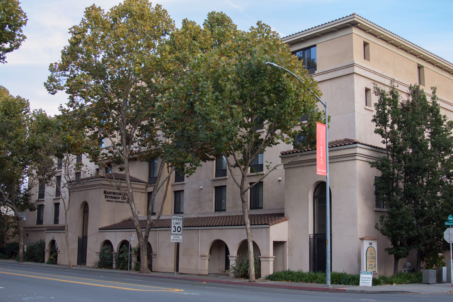 Front exterior of the Marymount Villa retirement center building with trees lining the sidewalk and a street in front.