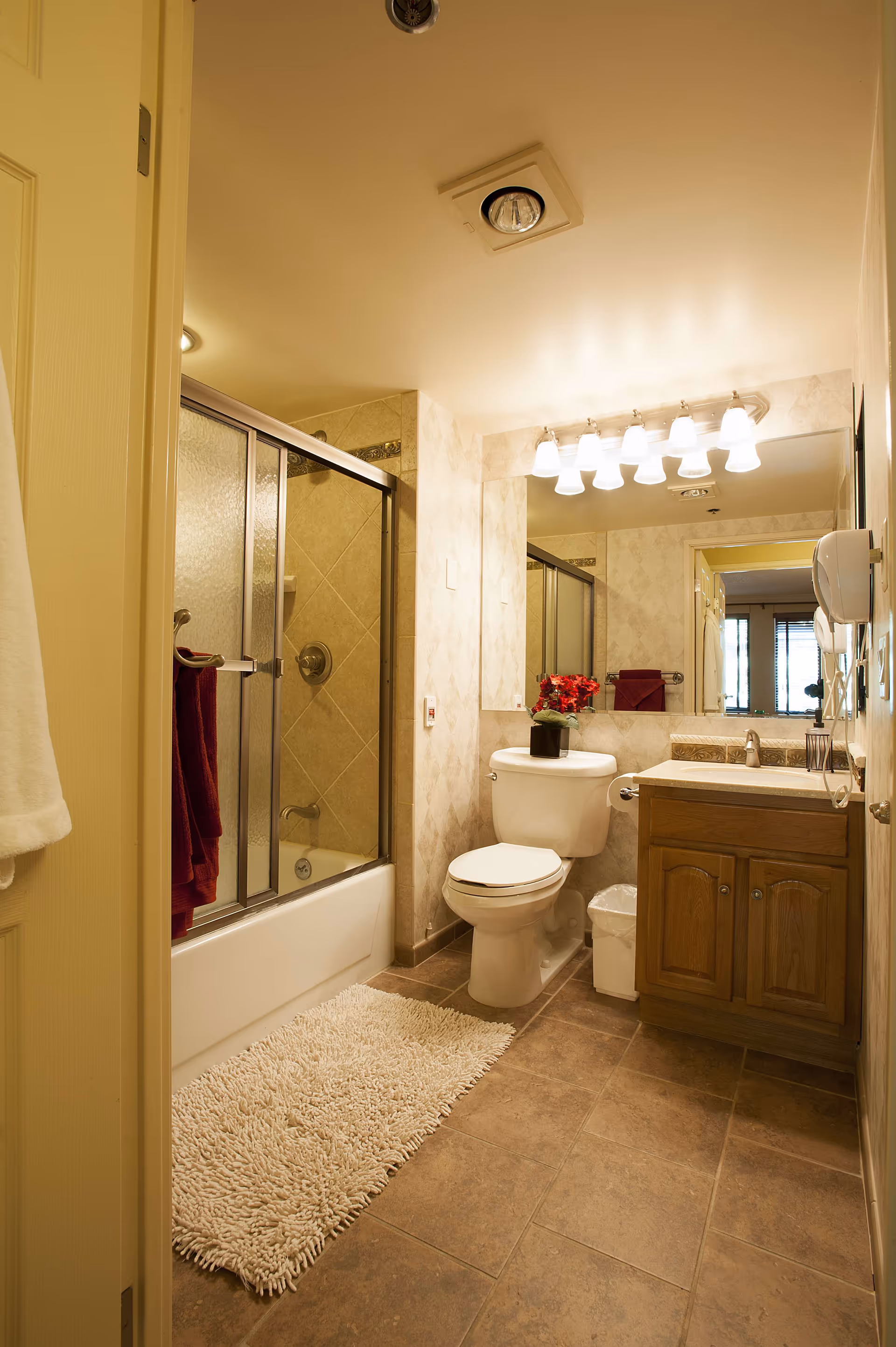 A clean, well-lit bathroom with a bathtub and sliding glass doors, a toilet, and a vanity with mirror and lights.