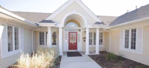 Front entrance of a light-colored senior living facility with red door and columns.