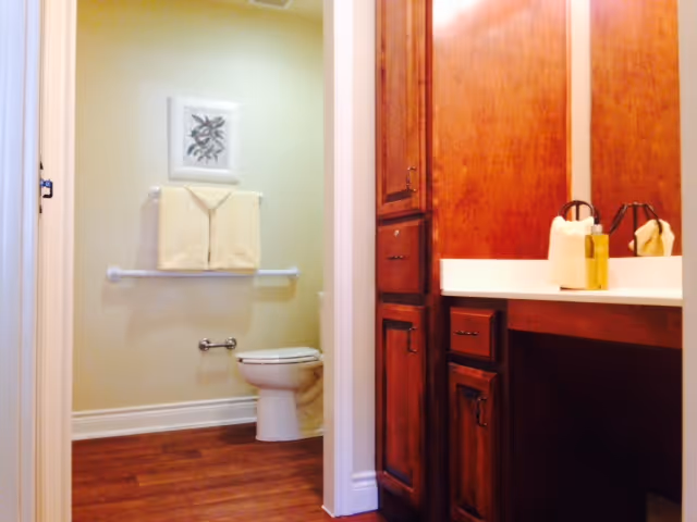 Bathroom interior with a wooden vanity and countertop on the right and a toilet, towel rack, and framed art on the left.
