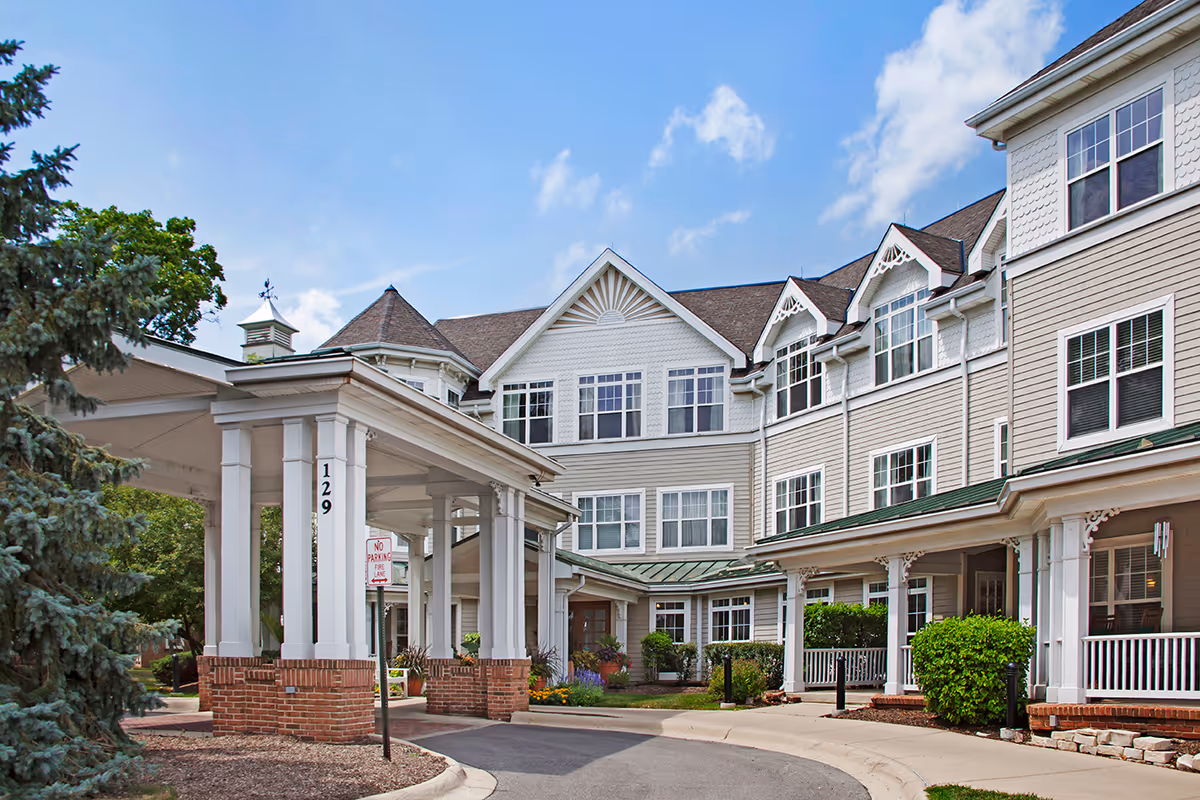 Front entrance of a multi-story senior living building with a covered porte-cochère and landscaped driveway.