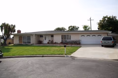 A single-story beige building with a front lawn, driveway, and attached garage.