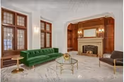 Elegant common room with a green velvet sofa, marble floor, ornate fireplace, and wood-paneled wall.
