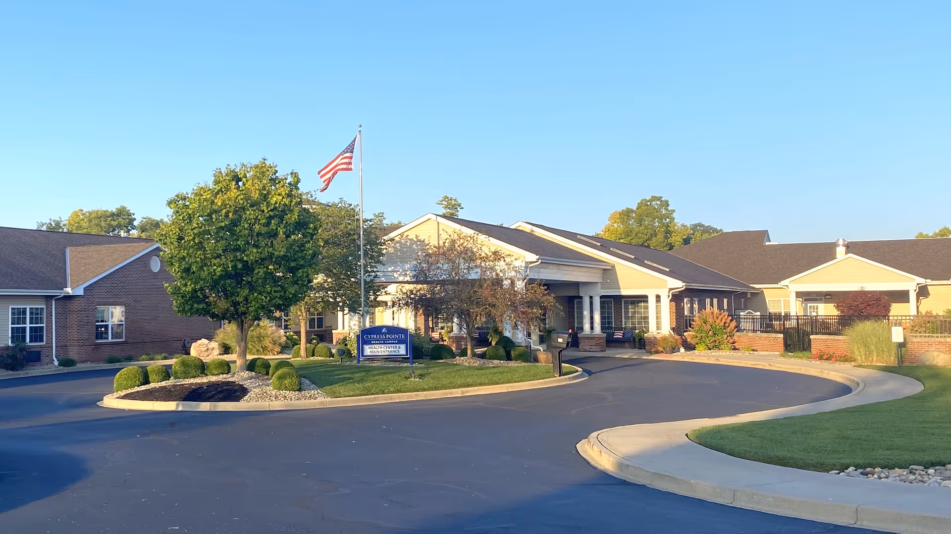 Front entrance of Cypress Pointe Health Campus with a circular driveway, flagpole, and landscaped grounds under a clear blue sky.