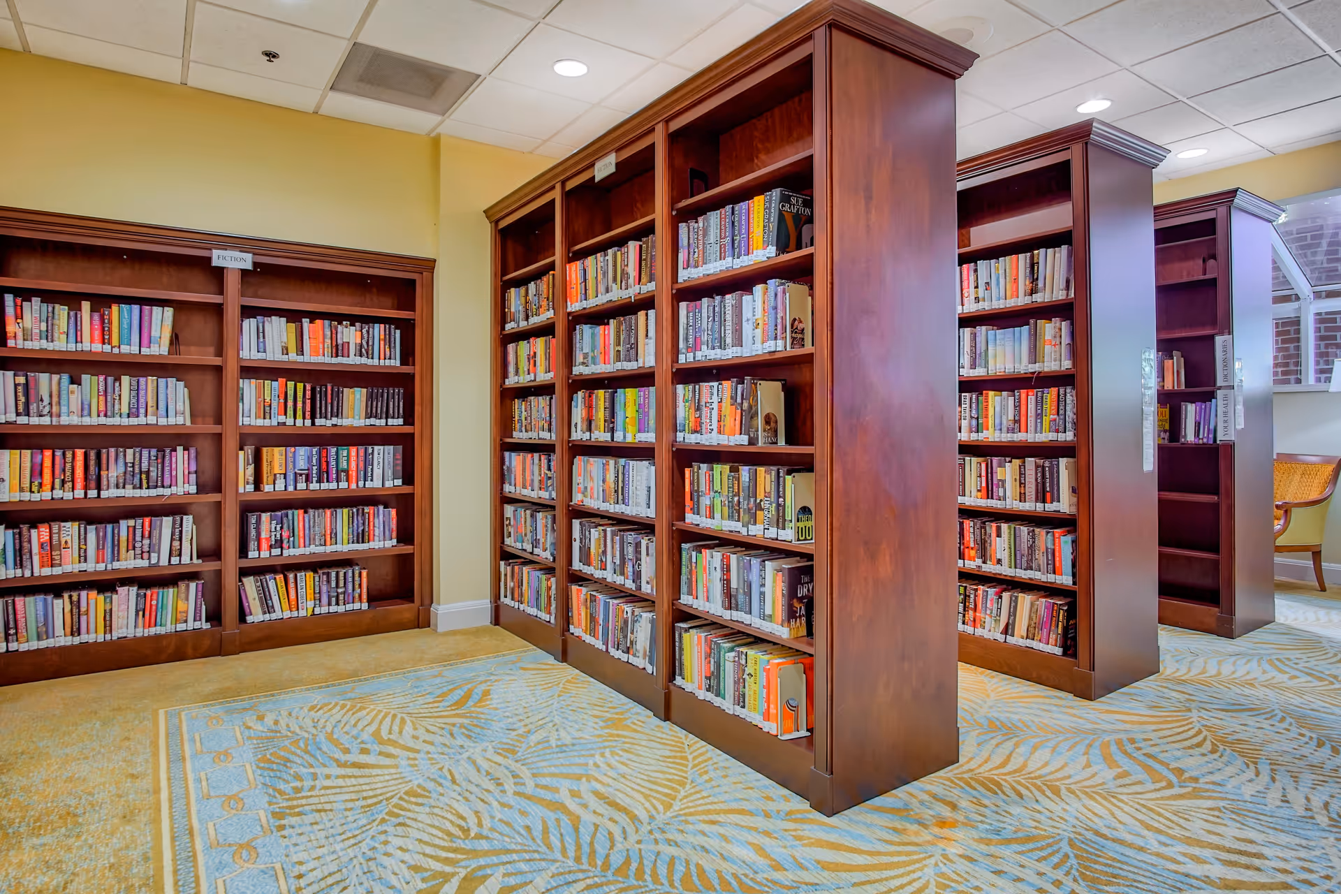 Interior library area with several wooden bookshelves filled with books and a patterned carpeted floor.