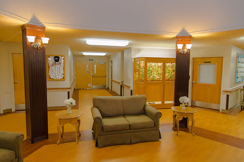 A small lounge area with a two-seat sofa flanked by side tables and decorative columns in a well-lit corridor.