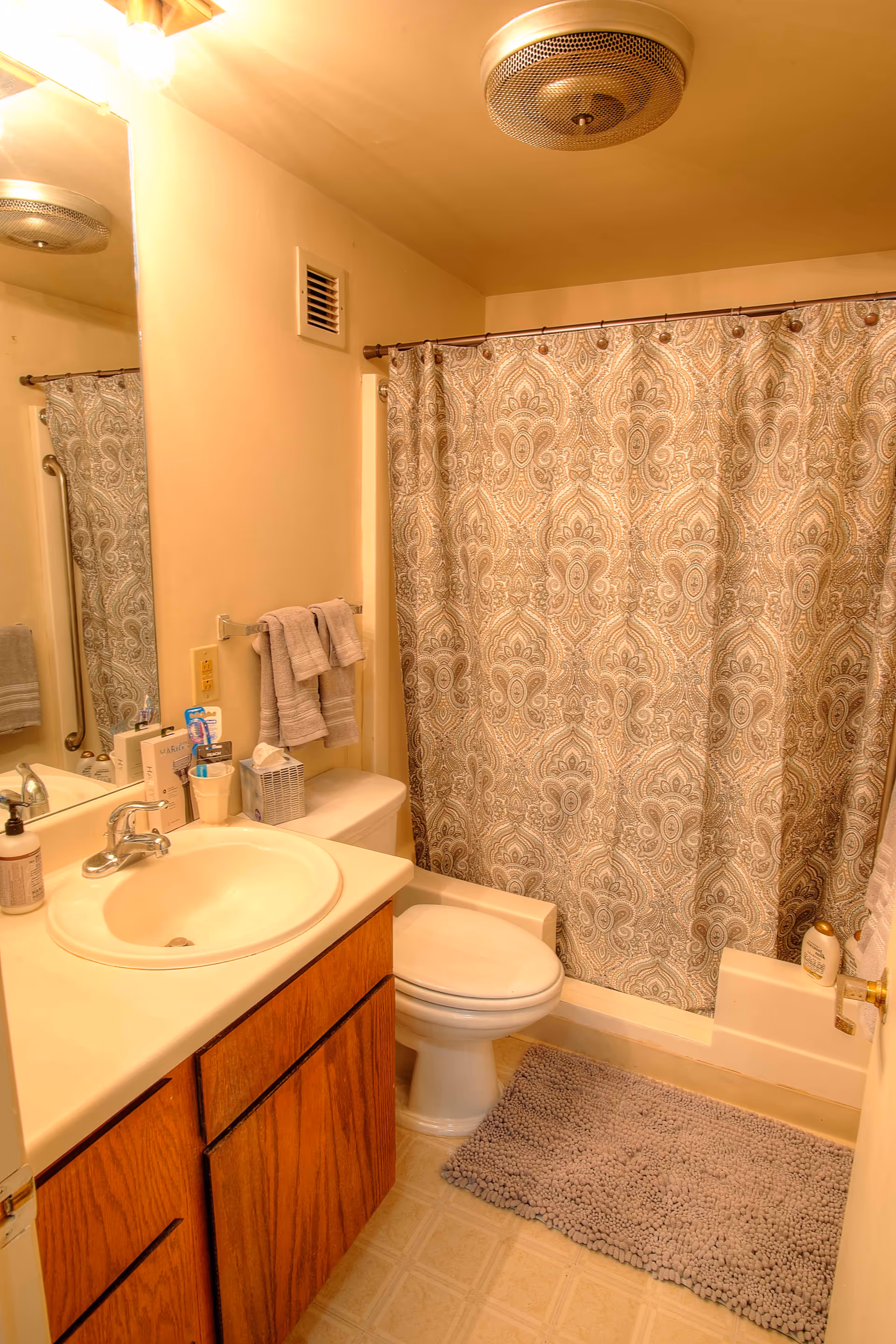 Small bathroom with a sink and wooden vanity, toilet, and a tub/shower behind a patterned curtain.