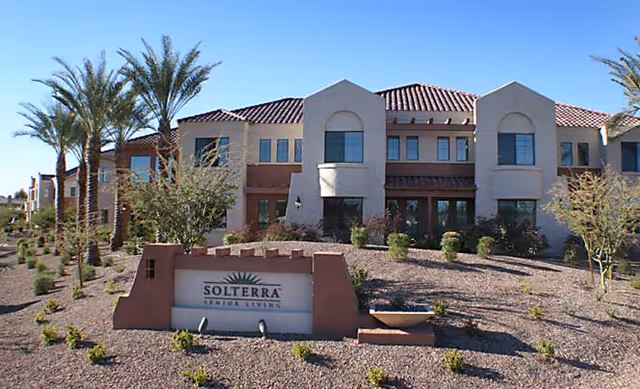 Exterior front view of Solterra senior living building with desert landscaping, palm trees, and a stone entrance sign.