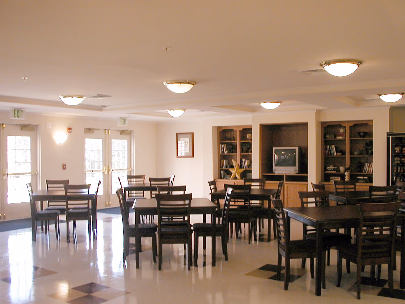 Spacious communal dining room with multiple wooden tables and chairs, built-in shelving and a TV at the back.