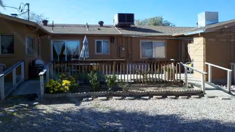 Exterior view of a senior living facility with a gravel courtyard and railing.