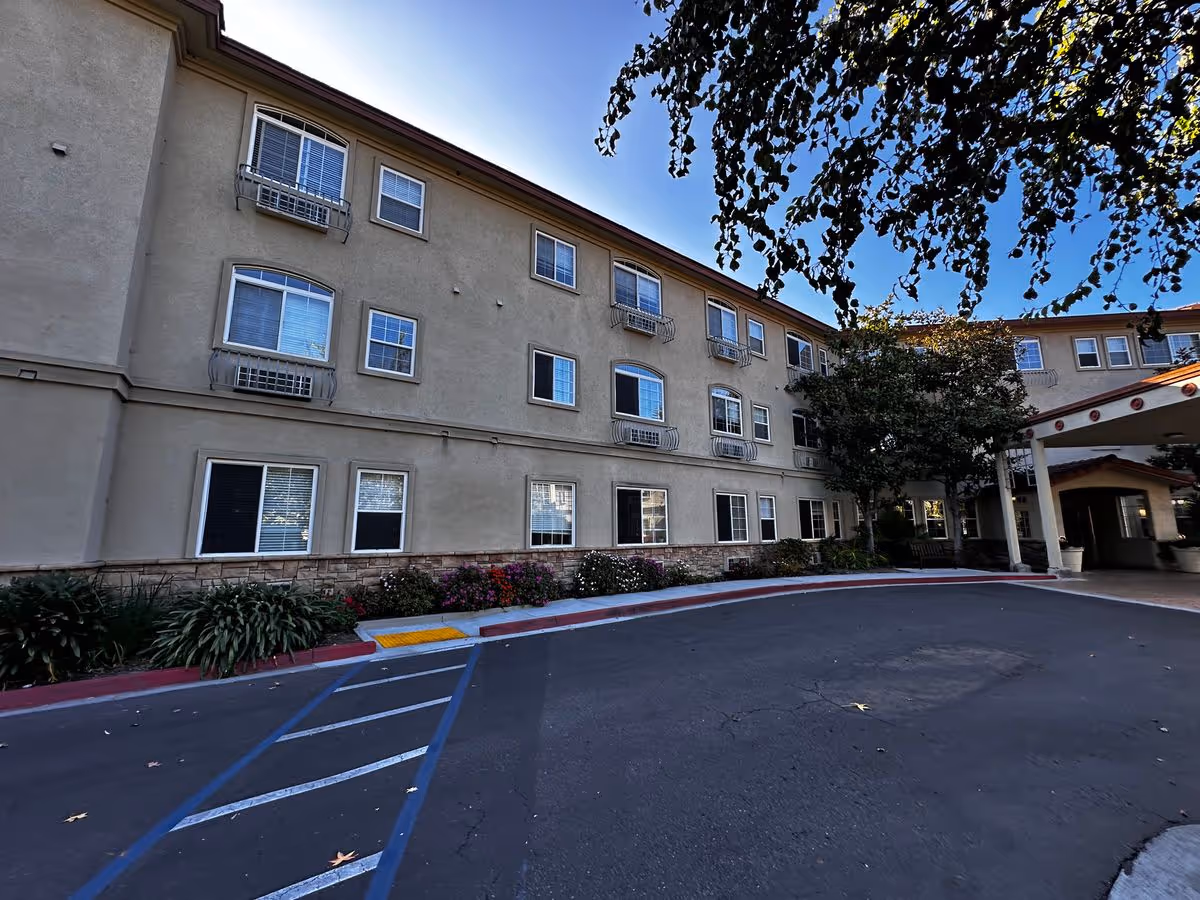 Front exterior of a three-story senior living building with a covered entrance, driveway, and landscaping.