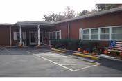 Single-story brick building entrance with a covered drop-off, parking spaces, pumpkins along the landscaping and an American flag by the windows.