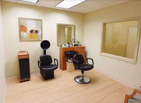 Small salon room with two styling chairs, a shampoo sink, mirror and cabinet in a light-colored interior.