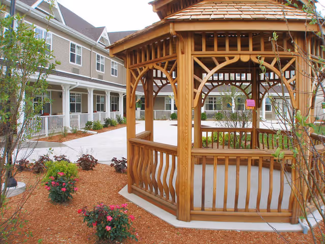 Wooden gazebo in a landscaped courtyard beside a multi-story residential building.