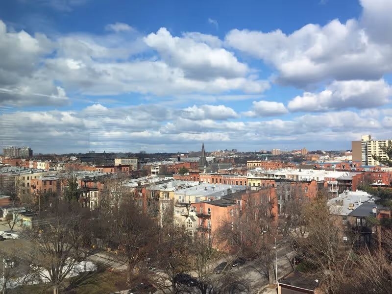 View over a residential neighborhood with multiple brick buildings and leafless trees under a partly cloudy blue sky.