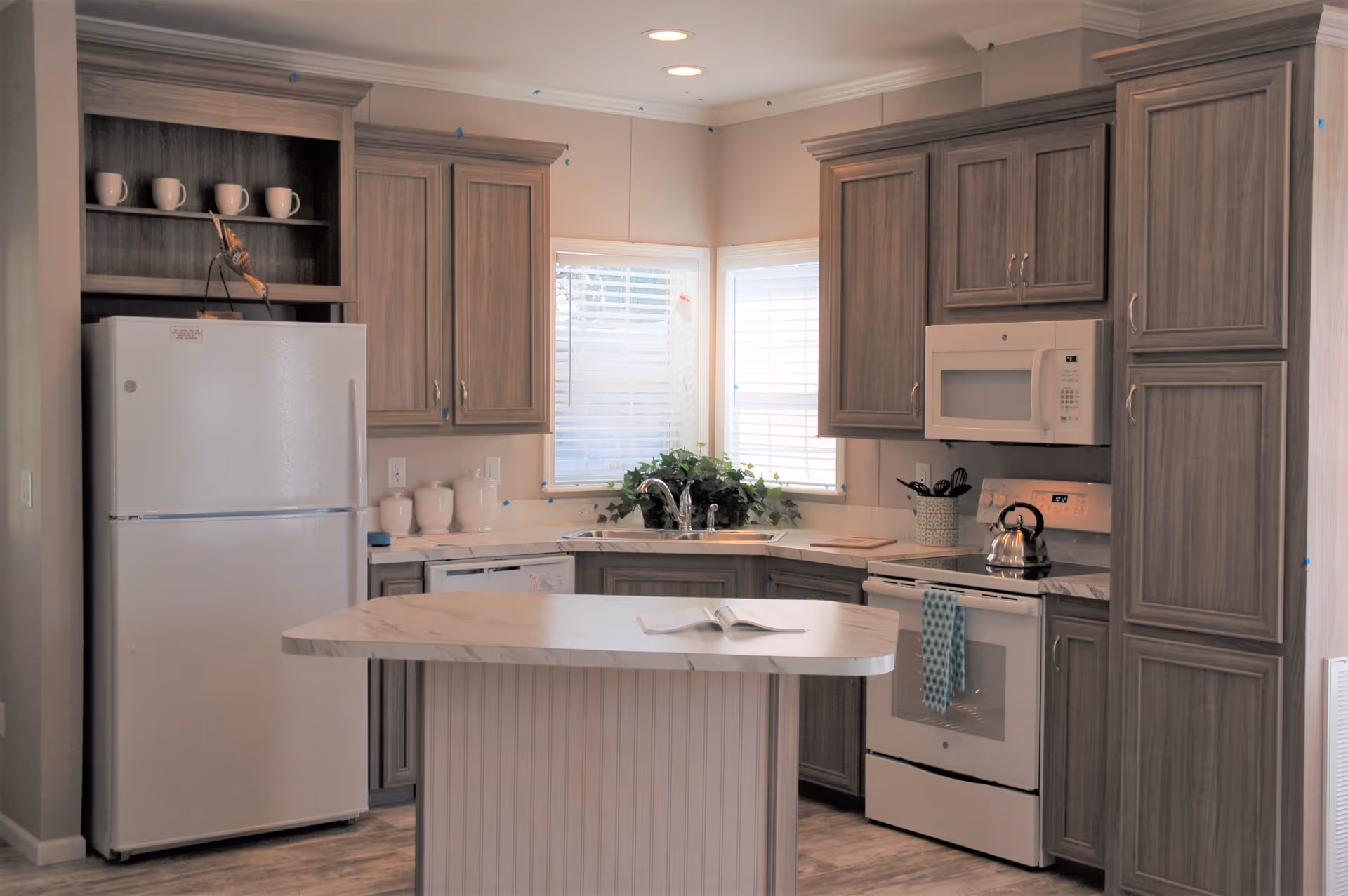 Well-lit kitchen with a central island, wood cabinets, white refrigerator and stove, and a window with blinds.