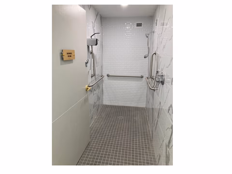 Accessible tiled shower room with grab bars and a shower room sign on the door.