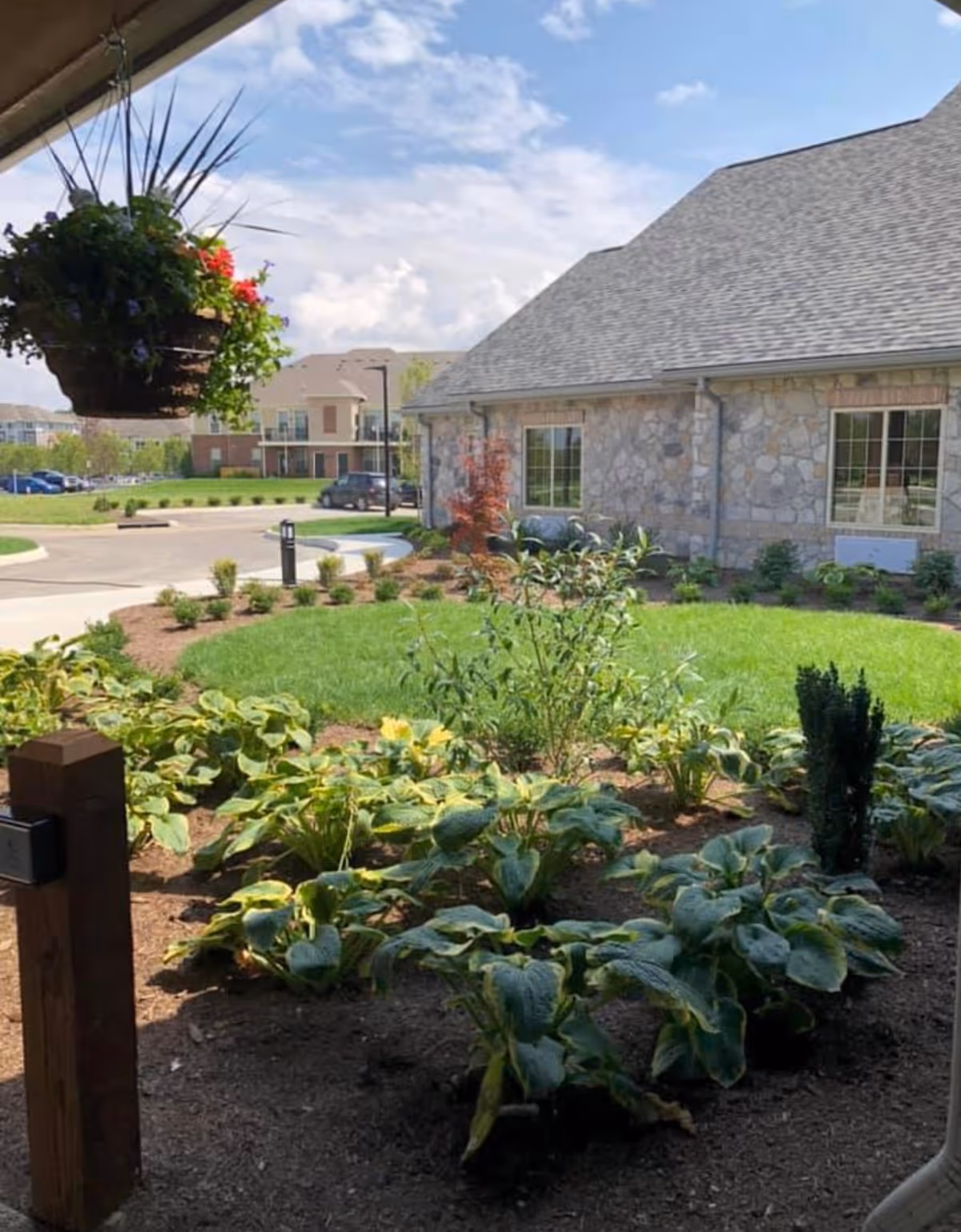 Landscaped garden and lawn outside a stone-faced building with a hanging flower basket.