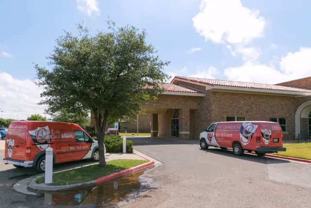 Two red vans with The Garrison logo parked outside a brick building with a covered entrance, under a partly cloudy sky.